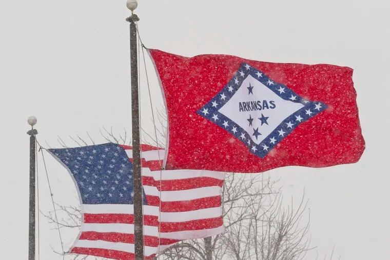 FILE - In this Feb. 1, 2011 file photo, an American and Arkansas flag blow in the wind as snow falls in Fayetteville, Ark.  An Arkansas House panel on Wednesday, March 20, 2019 rejected for a second time a proposal to change the meaning of a star on the state’s flag that currently represents the Confederacy, despite an endorsement from the Republican governor. (AP Photo/Beth Hall, File)
