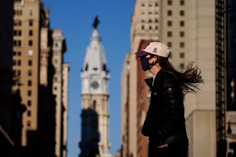 A woman wearing a face mask crosses Broad Street, Wednesday, Nov. 18, 2020, in Philadelphia. Pennsylvania is strengthening its mask mandate and will require out-of-state travelers to test negative for the coronavirus before arrival, health officials announced Tuesday, taking additional steps to address a sharp increase in infections and hospitalizations. (AP Photo/Matt Slocum)