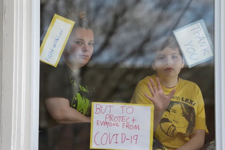 Janine McAlonan and her daughter Lexi, who has lymphoma, pose for a portrait in the window of their home in Philadelphia, PA on March 24, 2020. Lexi and her family are taking extra precautions because of her compromised immune system.