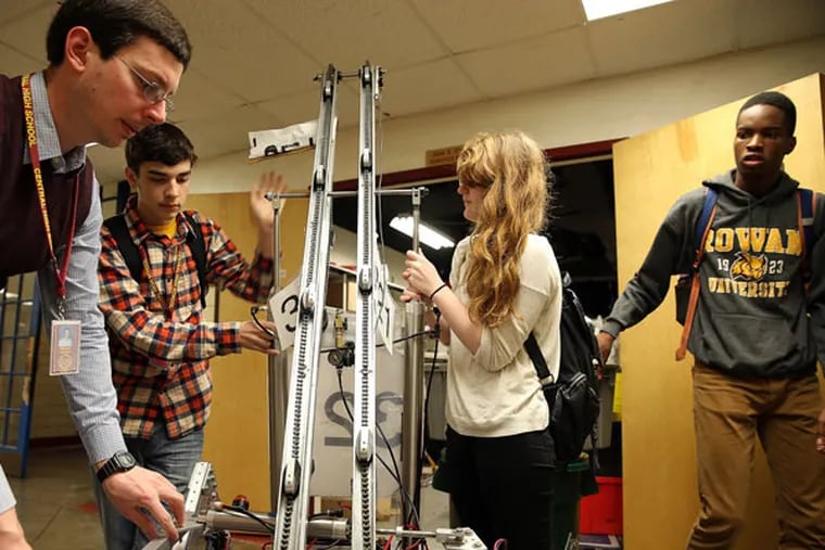 Central High students Evan Aretz, second from left, Maria Shayegan, center, and Stanley Umeweni, right, show off their robot with the help of teacher Michael Johnson, left, at Central High School in Philadelphia on April 14, 2015. ( DAVID MAIALETTI / Staff Photographer )