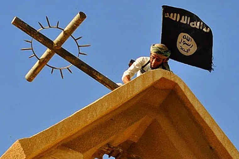 A member of ISIS holds the group's flag while dismantling a cross atop a church in Mosul, Iraq.