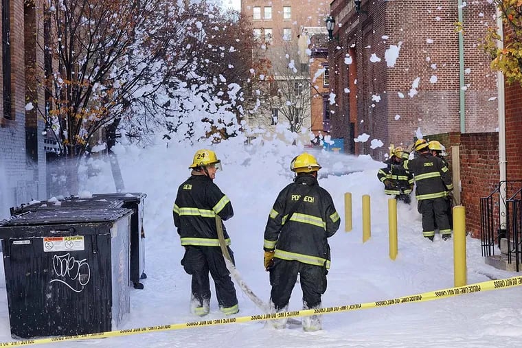 Firefighters work to wash down foam from the fire suppression system of a building on Juniper St. near Lombard Street