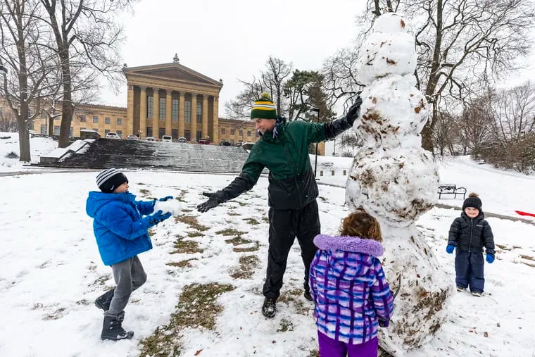 Brentley Long, 8, of Fishtown, hands Sean Beuche, of Northern Liberties, snow to add to the snowman they were buildingn behind the Philadelphia Museum of Art on Tuesday, Jan. 16, 2024.
