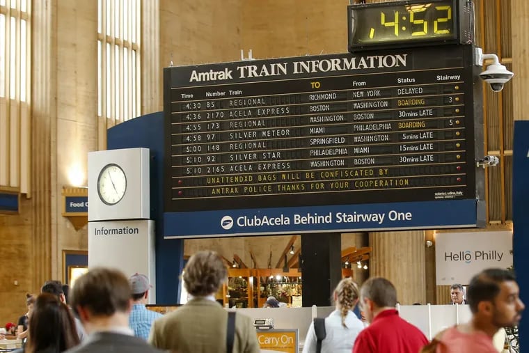 Amtrak riders at 30th Street Station stand near the train information board.
