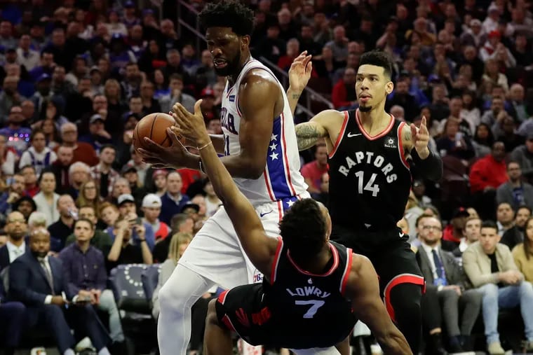 Sixers center Joel Embiid runs into a falling Toronto Raptors guard Kyle Lowry and past guard Danny Green during the second-quarter on Saturday, December 22, 2018 in Philadelphia.  YONG KIM / Staff Photographer