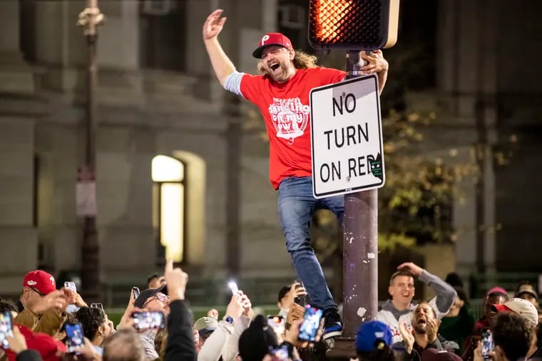 A fan celebrates the Philadelphia Phillies winning the National League Championship Series by climbing a pole on Broad Street south of City Hall on Sunday.