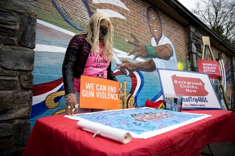 The Rev. Jeanette Davis, of D.I.V.A.S Ministry, an organization that advocates for gun violence prevention measures, signs a mural calling for background checks for gun buyers at Cobbs Creek Recreation Center in Philadelphia on Sunday.