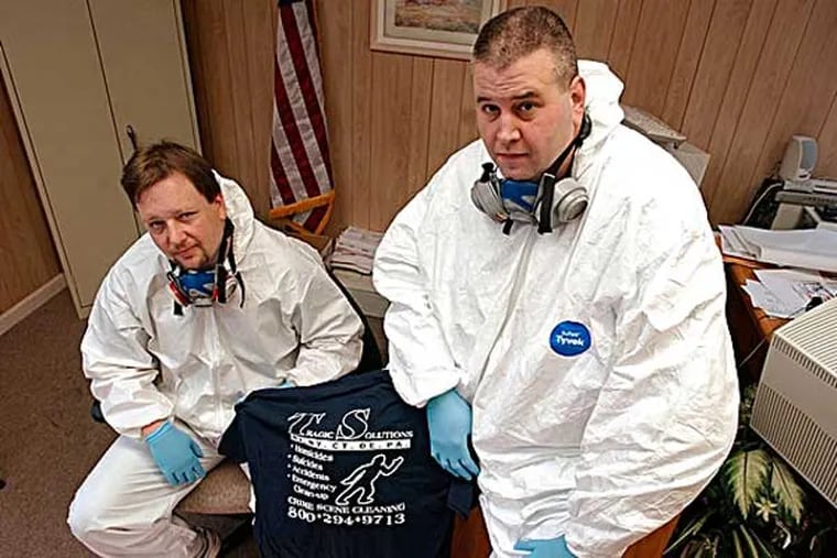 FILE PHOTO: Timothy Carroll, left, and Thomas Rohling co-owners of Tragic Solutions,  pose in protective biohazard coveralls at their office in Newark, N.J., Thursday, Dec. 16, 2004.  (AP Photo/Mike Derer)