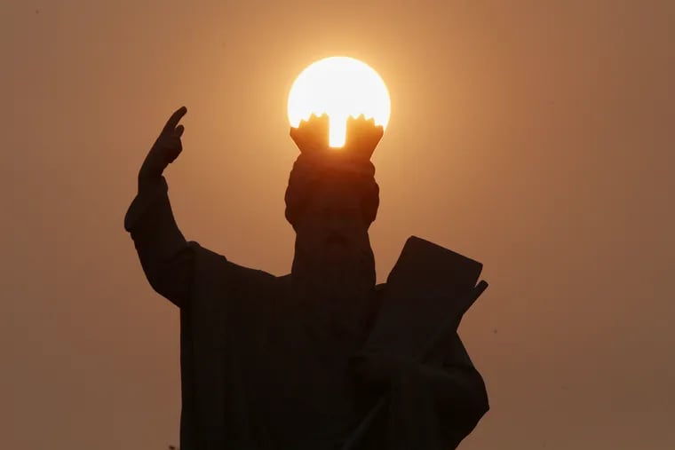 The sun sets against a reddish haze, caused by smoke from wildfires on the West Coast, as seen from behind part of the Catholic Total Abstinence Union Fountain in Philadelphia's Fairmount Park.