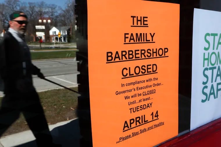 A pedestrian walks by The Family Barbershop, closed because of a Gov. Gretchen Whitmer executive order, in Grosse Pointe Woods, Mich.