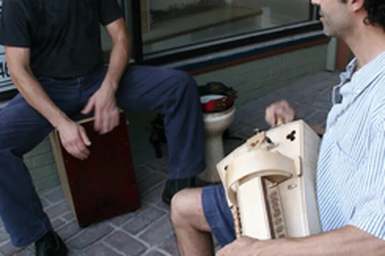 Bruce Panula (left) sits on and plays a caj&#0243;n as Tom Rozano plays hurdy-gurdy during the street festival.
