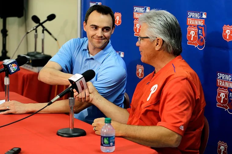 Philadelphia Phillies general manager Matt Klentak, left, shakes hands with manager Pete Mackanin as they talk about Mackanin's new two-year contract before a spring training baseball game between the Phillies and the Toronto Blue Jays Friday, March 25, 2016, in Clearwater, Fla.