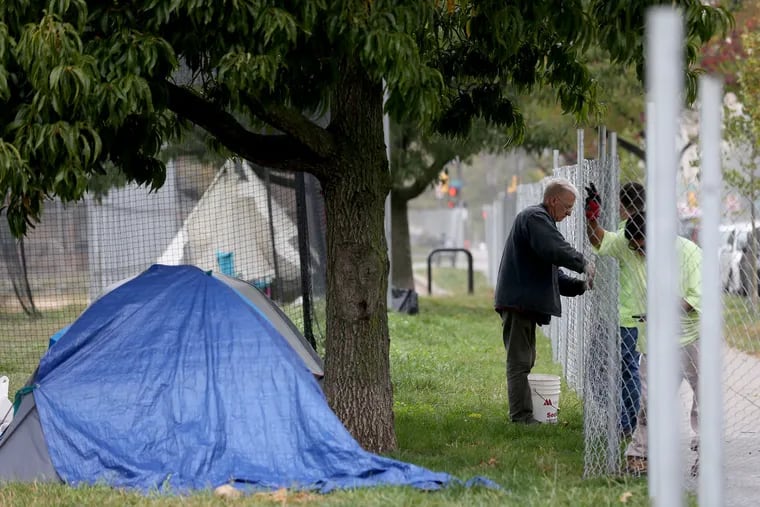 Joe Waldron (left), of Bustleton Services Inc., installs a section of a 2,200-foot fence around the homeless encampment site on the Benjamin Franklin Parkway on Monday.