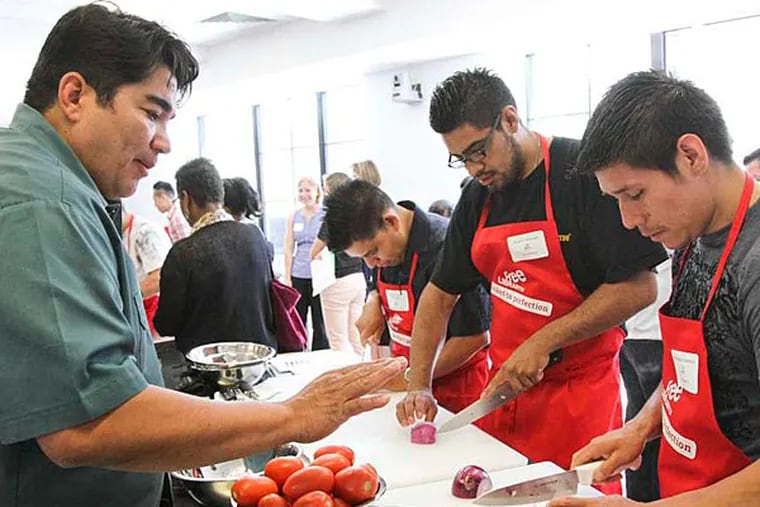 Chef Jose Garces (left) offers knife-skill tips to future culinary students (left to right) Juventino Martinez, Javier Aguilar, and Jeronimo Cabrera. (David M Warren/Staff Photographer)