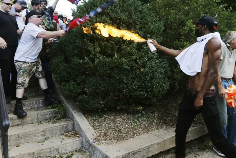 A counterdemonstrator uses a lighted spray can against a white nationalist demonstrator at the entrance to Lee Park in Charlottesville, Va.