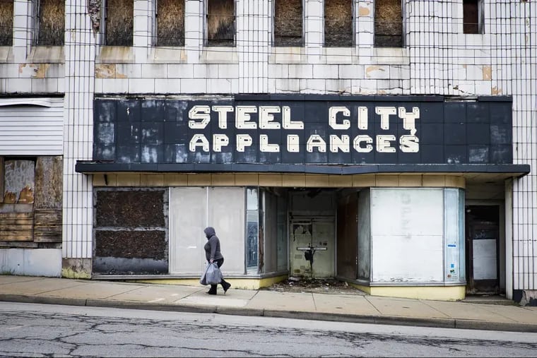 A woman walks along one of the main streets in Clairton, Pa., past the old Steel City Appliances, where many of the storefronts are boarded up.