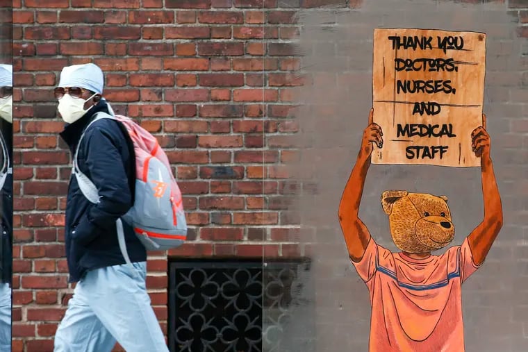A pedestrian walks past a painting thanking doctors, nurses, and medical staff members near the Hospital of the University of Pennsylvania on Thursday, April 23, 2020.