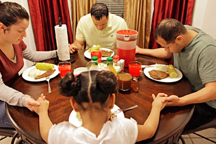Edwin Sanabria (right) prays before dinner with his new family: brother Robert, sister-in-law Toni Vega, and niece Izzy, 6, in Fayetteville, N.C. He and three others were found imprisoned in a dank basement in Tacony in October. (Ted Richardson / Associated Press)
