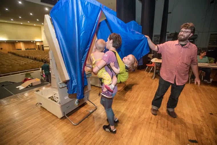 Vera Dugan, 18 months, right, holds on tight to Bridget Huffman, center, as she holds her son Drew Huffman, 20 months, left, as they all go into the voting booth together, on the stage of the auditorium of South Philadelphia High School on May 15, 2018. Nazim Karacaa, right, holds open the blue curtain so Huffman and her brood can enter to vote in the primary election in the 39th District in South Philadelphia.