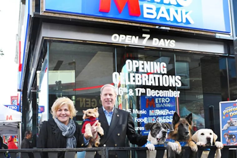 Vernon and Shirley Hill, with dogs, outside the new Metro Bank P.L.C. branch in Hounslow, London. Shirley Hill's company designs the bank branches her husband builds. (Philip Hartley / For the Inquirer)