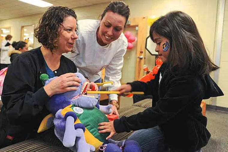 Renee Batdorf (leff) and Dawn Hampton,  both alumni of Burlington County College, use toys to show 5-year-old Sophia Gonzalez how to brush her teeth during the school's Give Kids a Smile Day on February 1, 2013. ( RON TARVER / Staff Photographer )