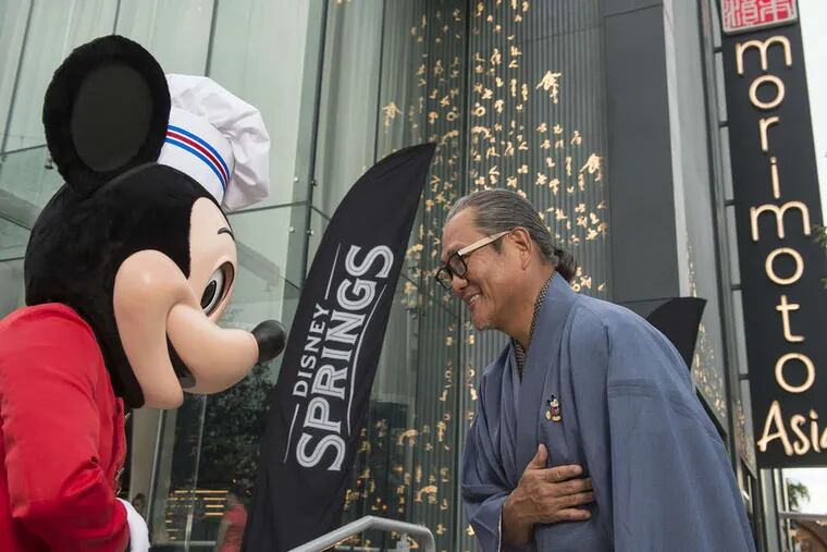 Mickey Mouse and chef Masaharu Morimoto exchange a greeting at the new Disney Springs complex at Walt Disney World Resort in Florida. The shopping and dining spot is scheduled for completion in 2016. When done, the complex will have more than 150 shops and restaurants, including a new Morimoto offering, and park-like scenery.