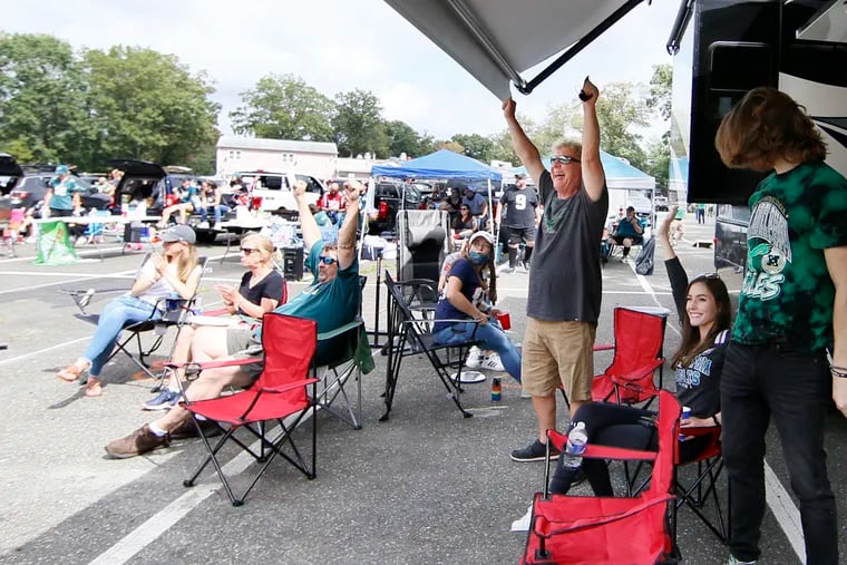 Eagles fan Jeff Asher (standing) of Skippack, Pa. raises his arms and cheers for the Eagles second touchdown while watching the Phila. Eagles season opener at Innovative Catering Concepts in Williamstown, N.J. on Sept. 13, 2020. Eagles fans gather at a South Jersey catering company for the first game of the Eagles season. For $40 a car, folks can watch the game on a giant screen outdoors and tailgate with their family and friends.