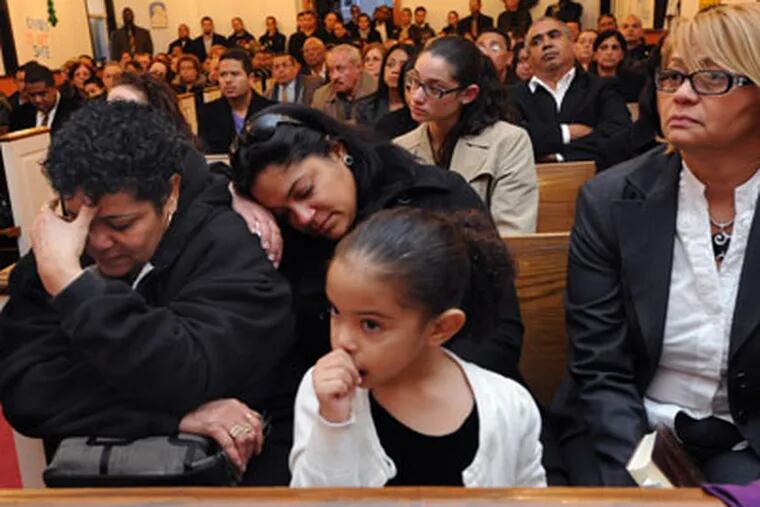 At Thursday’s funeral for Miguel Almonte, St. Andrew’s Episcopal Church in Camden was decorated with signs decrying the city’s violence and calling for more police officers. Almonte was slain Monday at his bodega. The mother of his children, Evelyn Martinez, (center) holds their daughter, Emely, 3. At left is his cousin Daucelina Santos Almonte. (April Saul / Staff Photographer)