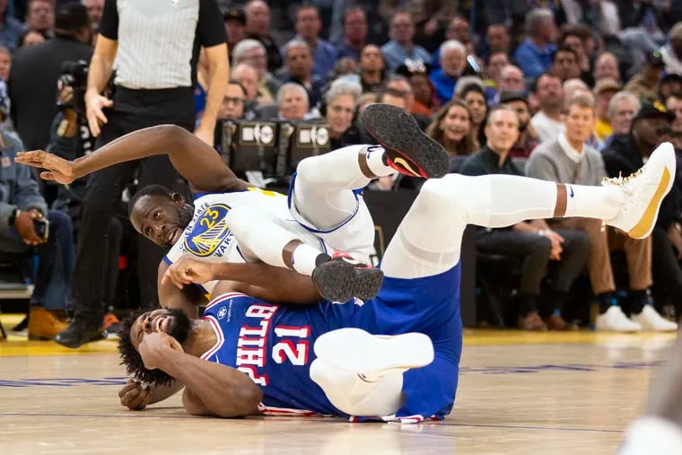 Golden State Warriors forward Draymond Green (23) falls over Philadelphia 76ers center Joel Embiid (21) on an offensive foul by Embiid during the first half of an NBA basketball game on Tuesday in San Francisco.