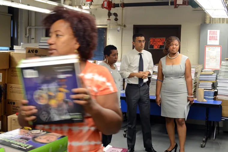 Staffers Kim Morrow (left) and Mayra Rojas-Rutledge (front) open boxes of new textbooks at Woodrow Wilson HS September 6, 2013, as Paymon Rouhanifard (rear, center), the first state-appointed Superintendent of the Camden School District, takes a tour of the school with co-principals Deborah Olusa (rear, right), principal for grades 11-12, and Lisa Thomas (rear, left) principal for grades 9-10.  (TOM GRALISH / Staff Photographer)