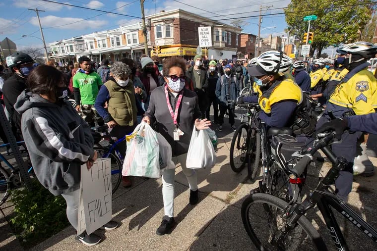 An unidentified woman tries to squeeze between protesters and police as she carries groceries.  Protesters gathered on Oct. 31, 2020, in West Philadelphia near the site where Walter Wallace, Jr. was shot.  The unrest was sparked by the fatal shooting of Walter Wallace, Jr. by police earlier in the week.