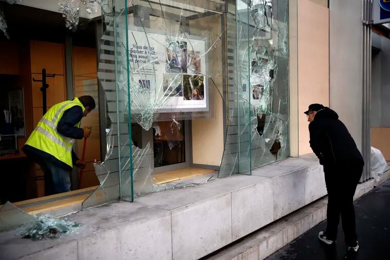 A worker clears debris in a bank as a man watches through smashed windows, in Paris, Sunday, Dec. 9, 2018. Paris monuments reopened, cleanup workers cleared debris and shop owners tried to put the city on its feet again Sunday, after running battles between yellow-vested protesters and riot police left 71 injured and caused widespread damage to the French capital. (AP Photo/Christophe Ena)