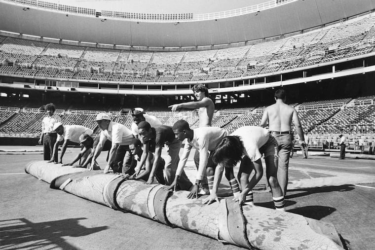Grounds crew take up the AstroTurf at third base in Veterans Stadium to convert the field from football to baseball on Aug. 1, 1981.