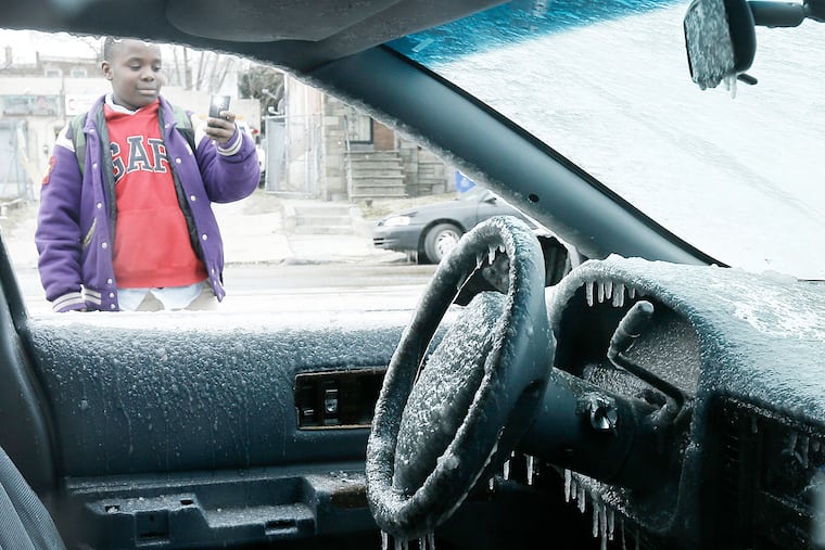 Donovan Jackson, 12, takes a photo of a car encased in ice after a fire hydrant broke on North 63rd Street between Girard and Haverford Avenues in Philadelphia on Friday.
