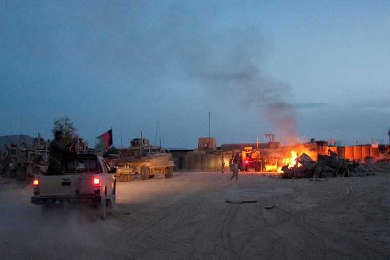 An Afghan National Army pickup truck passes parked U.S. armored military vehicles, as smoke rises from a fire in a trash burn pit at Forward Operating Base Caferetta Nawzad, Helmand province south of Kabul, Afghanistan. The House is poised to pass legislation that would dramatically boost health care services and disability benefits for veterans exposed to burn pits in Iraq and Afghanistan.