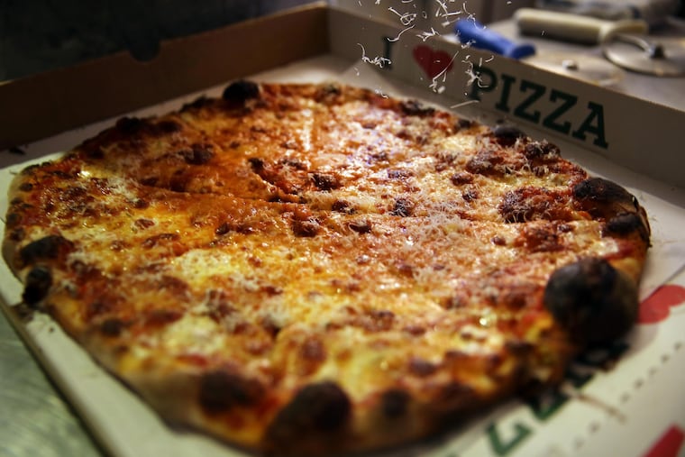 Joe Beddia of Pizzeria Beddia grating cheese over a pizza at his old shop on Girard Avenue.