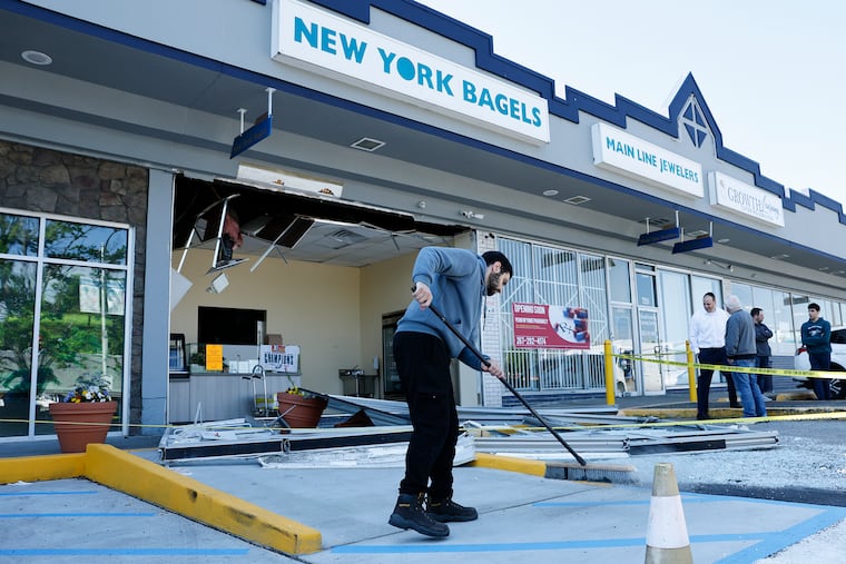 New York Bagels employee Tareq Kayyali sweeps glass from the parking lot after an explosion at the Overbrook Park kosher bagel shop at 7555 Haverford Ave. on Sunday.