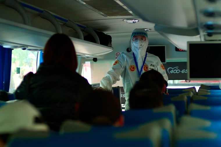 A government worker in full protective gear speaks on a bus to passengers recently arrived from Wuhan about an imminent medical screening in Beijing, China, Wednesday, April 15, 2020. Wuhan, the city at the center of the global coronavirus epidemic, lifted a 76-day lockdown and allowed people to leave for destinations across China.