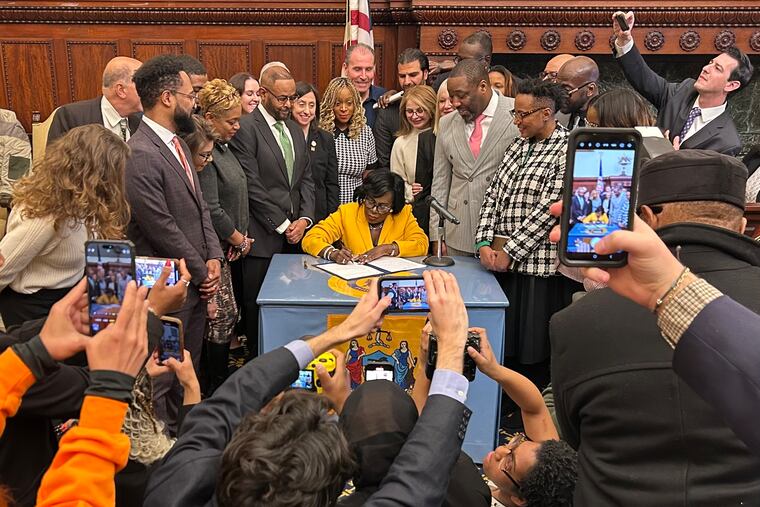 Mayor Cherelle L. Parker signs an executive order relating to her goal of building or preserving 30,000 affordable housing units. Angela D. Brooks, standing next to Council President Kenyatta Johnson, will lead that mission.