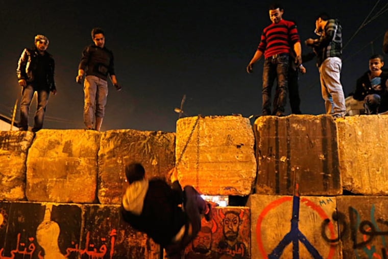 Protesters dismantle a wall guarding the presidential palace during a demonstration in Cairo. Arabic writing on the wall reads, "Killing me won't bring back your regime." PETR DAVID JOSEK / Associated Press