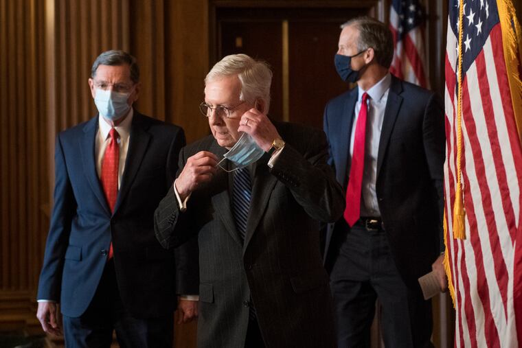 Senate Majority Leader Mitch McConnell of Ky., removes his face mask as he arrives with Sen. John Barrasso, R-Wyo., left, and John Thune, R-S.D., right, for a news conference with other Senate Republicans.