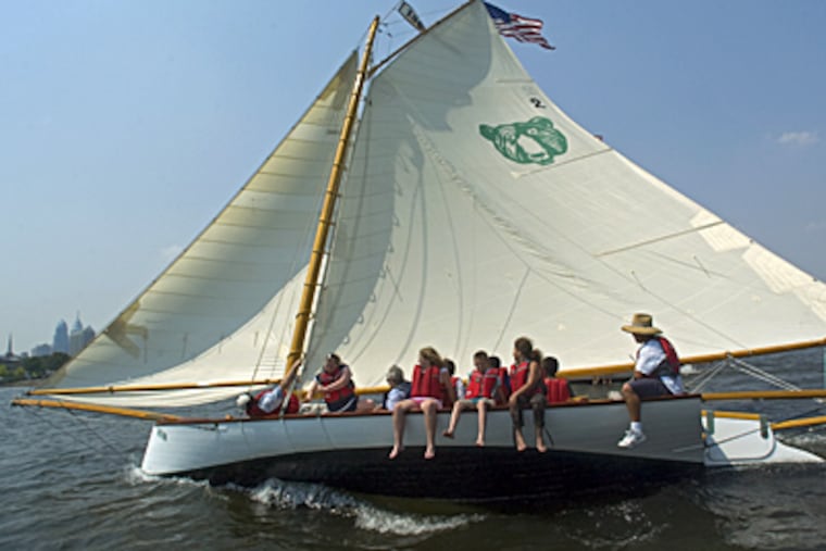 Maritime Academy Charter High School students sit on a gunwhale of the Bear racing boat while sailing on the Delaware River. The sandbagger boat is on display at the Independence Seaport Museum until today.