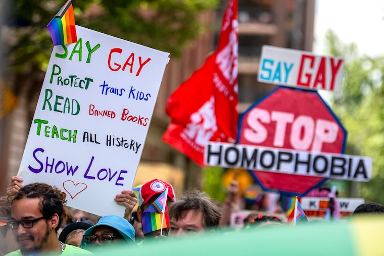 Signs countering the nationwide attack on LGBTQ people and their rights are carried during the march along Walnut Street in Center City on June 4, 2023. Since the election of Donald Trump in November, many LGBTQ people have expressed concerns that the incoming administration will further roll back a wide set of their rights, write the authors.
