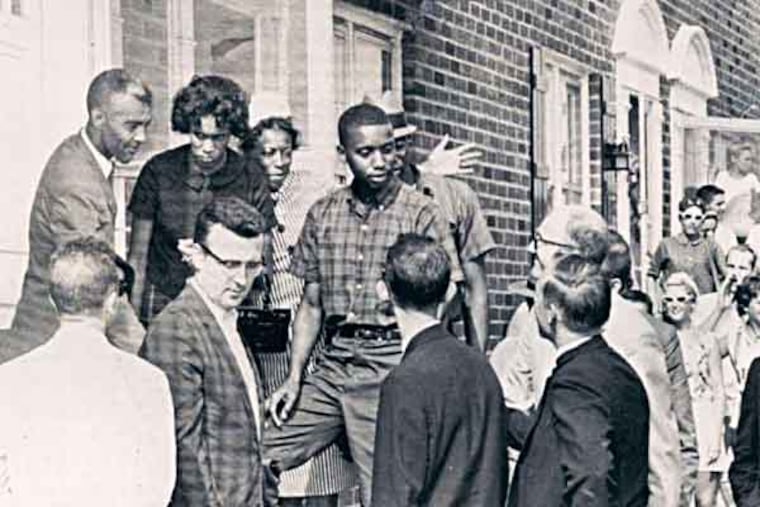 Horace Baker (center, in checkered shirt) and his wife, Sarah (second from left), left, pause at the door of their new home in an all-white neighborhood in Folcroft, trailed by a crowd. They moved in under protection from the state police in 1963. Associated Press, file