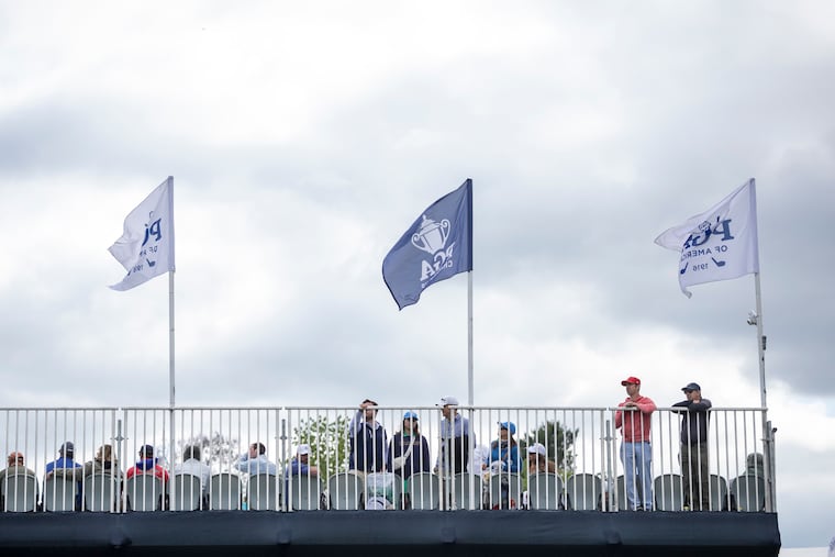 As winds whip the flags, brothers Peter (left) and Nick Fisk of Berwyn watching the action at Aronimink on Thursday. Wnds will be brisk Friday afternoon, but the weather is about to improve.