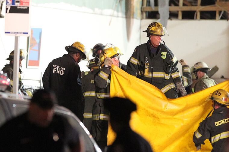 The death toll in up to six. Fire fighters hold up a yellow tarp as they prepare to remove another body from the collapsed building at 22nd and Market Sts. ( CHARLES FOX / Staff Photographer )