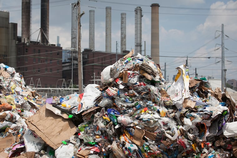 Smokestacks rise behind waste piled high at Republic Services' processing plant in the Gray's Ferry neighborhood of Philadelphia, Pa., on the afternoon of Tuesday, July 17, 2018. MAGGIE LOESCH / Staff Photographer