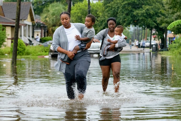 Jalana Furlough carries her son Drew Furlough as Terrian Jones carries Chance Furlough on Belfast Street near Eagle Street in New Orleans after flooding from a tropical wave system in the Gulf Mexico that dumped lots of rain in Wednesday, July 10, 2019. (AP Photo/Matthew Hinton)