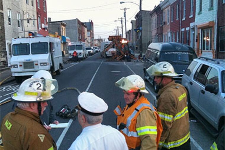 Firefighters confer Thursday while crews from Philadelphia Gas Works tried to repair a leaking gas main under the 3000 block of North Fifth Street in the city's Fairhill section. (Bob Moran / Staff Photographer)