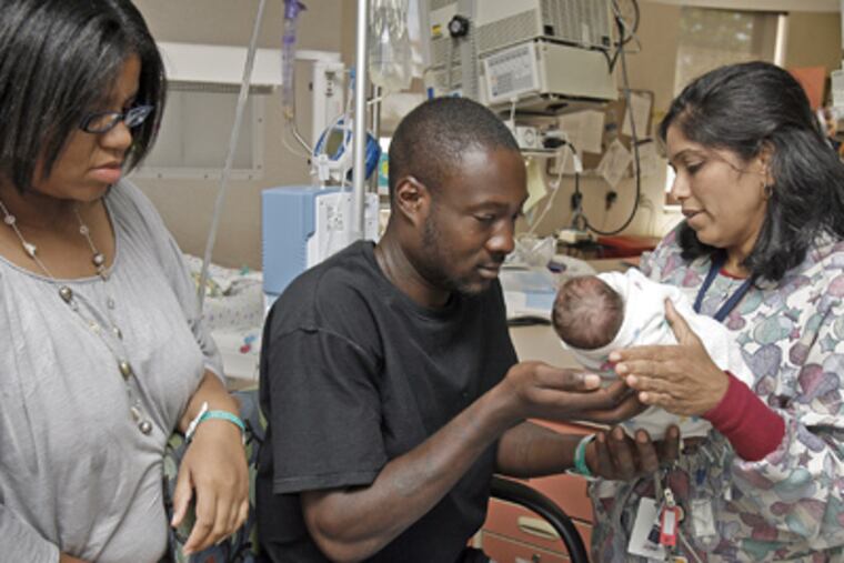 Heena Patel, Clinical Coordinator at NICU, hands Quinzel Kane Jr. very carefully to the father, Quinzel Kane Sr., while the mother, Charmaine Harris (left) watches. (Akira Suwa / Staff Photographer)
